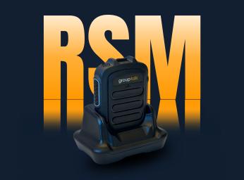 Bluetooth push-to-talk microphone docked in desktop charger.