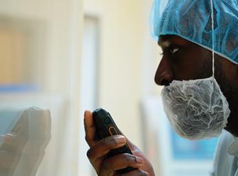 Worker in pharmaceutical facility using PTT to talk to team.