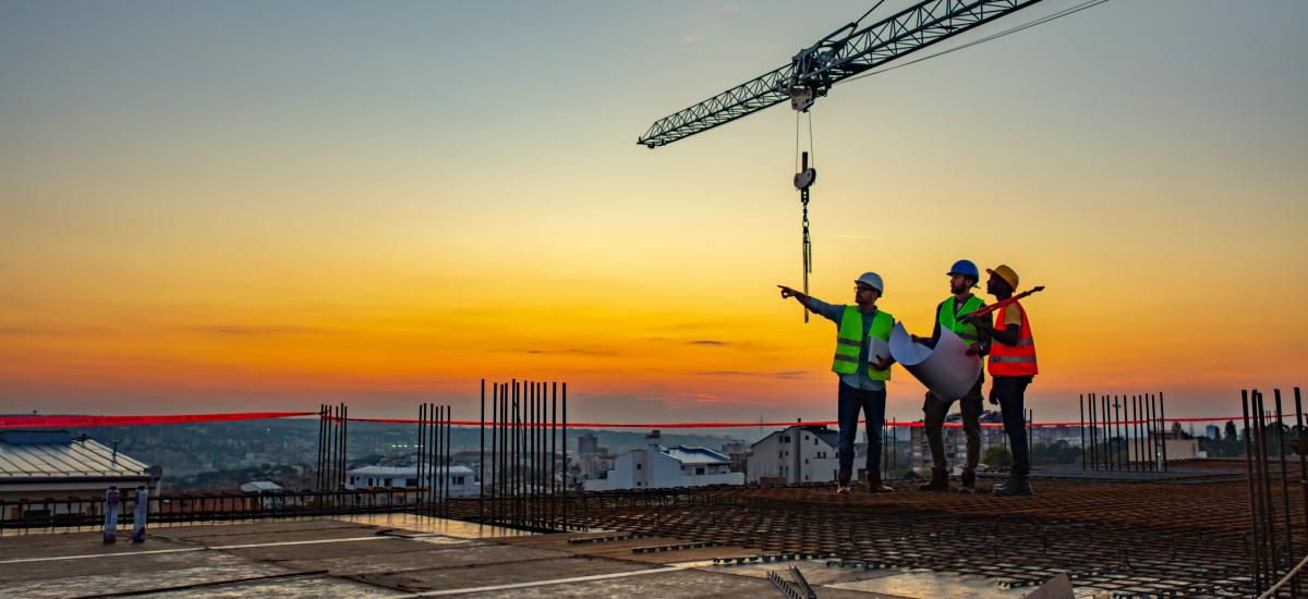 Three construction workers on rooftop during sunset.