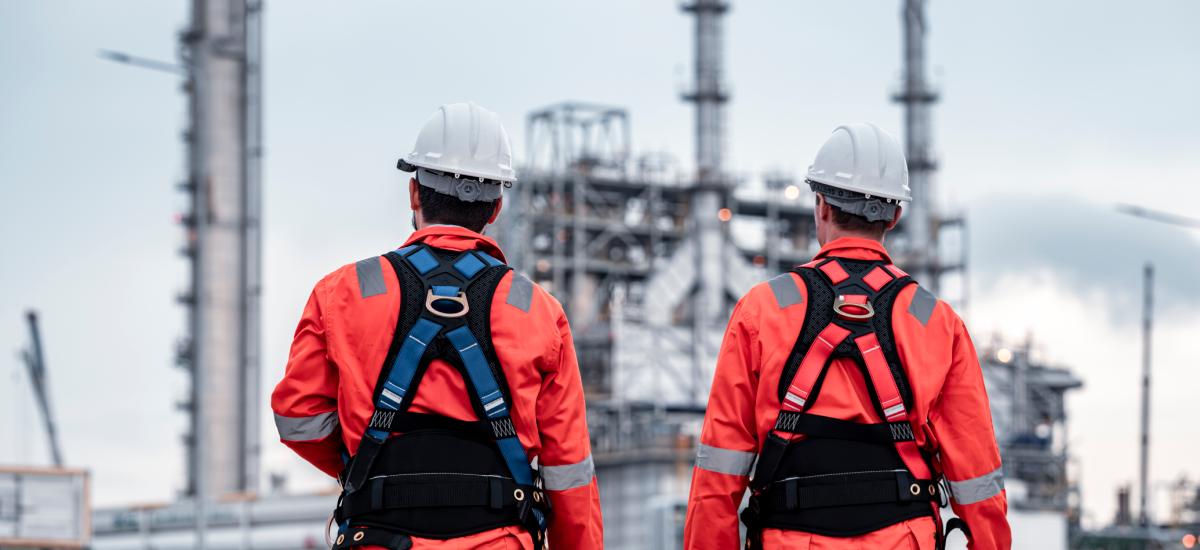 Construction engineers checking plans and using radios at refinery site.