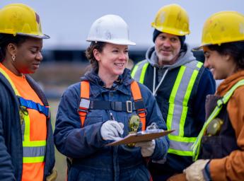 Group of four workers on construction site discussing plans, one using iPad.